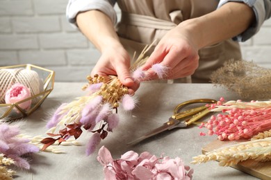 Florist making bouquet of dried flowers at grey stone table, closeup