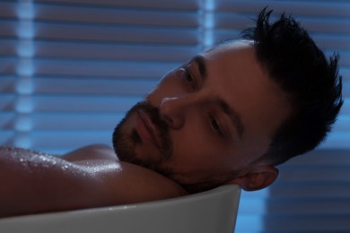Photo of Upset man thinking about something in bathtub at night. Loneliness concept