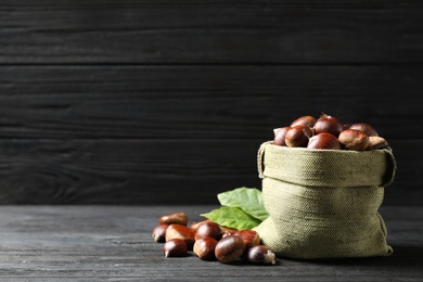 Photo of Fresh sweet edible chestnuts on black wooden table. Space for text