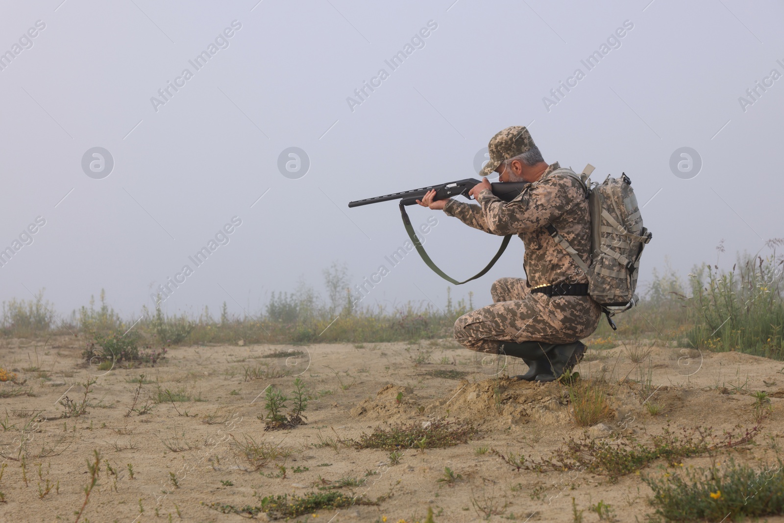 Photo of Man wearing camouflage and aiming with hunting rifle outdoors. Space for text