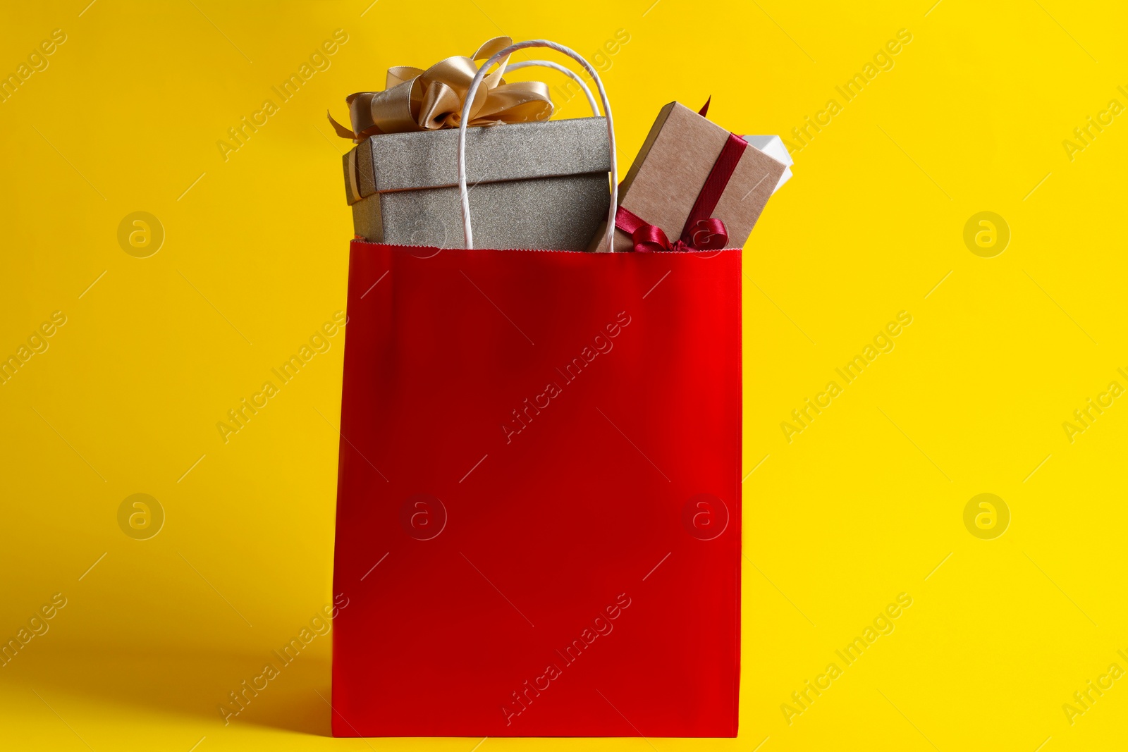 Photo of Red paper shopping bag full of gift boxes on yellow background
