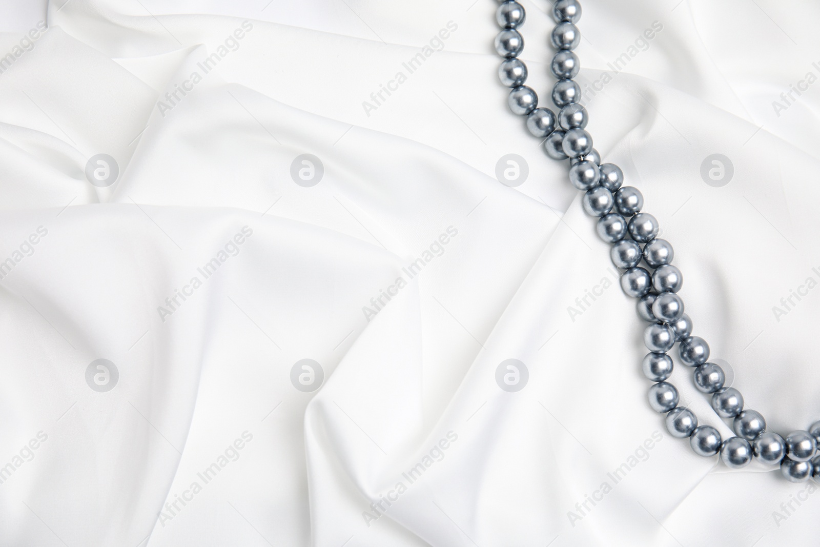 Photo of Beautiful pearls on white silk, top view. Space for text