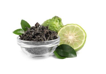 Photo of Dry bergamot tea leaves in glass bowl and fresh fruits on white background