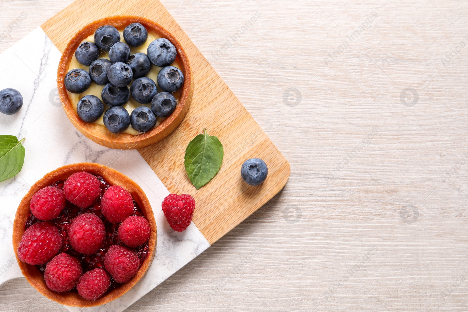 Photo of Tartlets with different fresh berries on light wooden table, top view and space for text. Delicious dessert