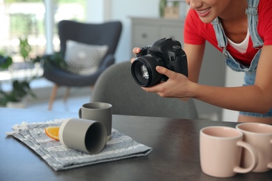 Photo of Young photographer taking picture of cups at table indoors, closeup