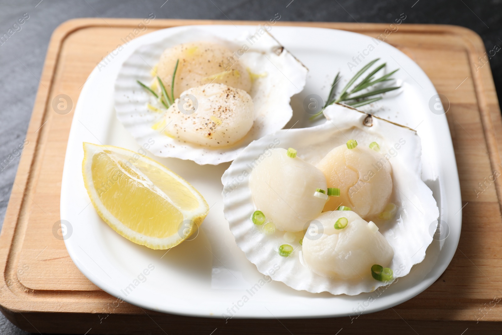 Photo of Raw scallops with green onion, rosemary and lemon on dark table, closeup