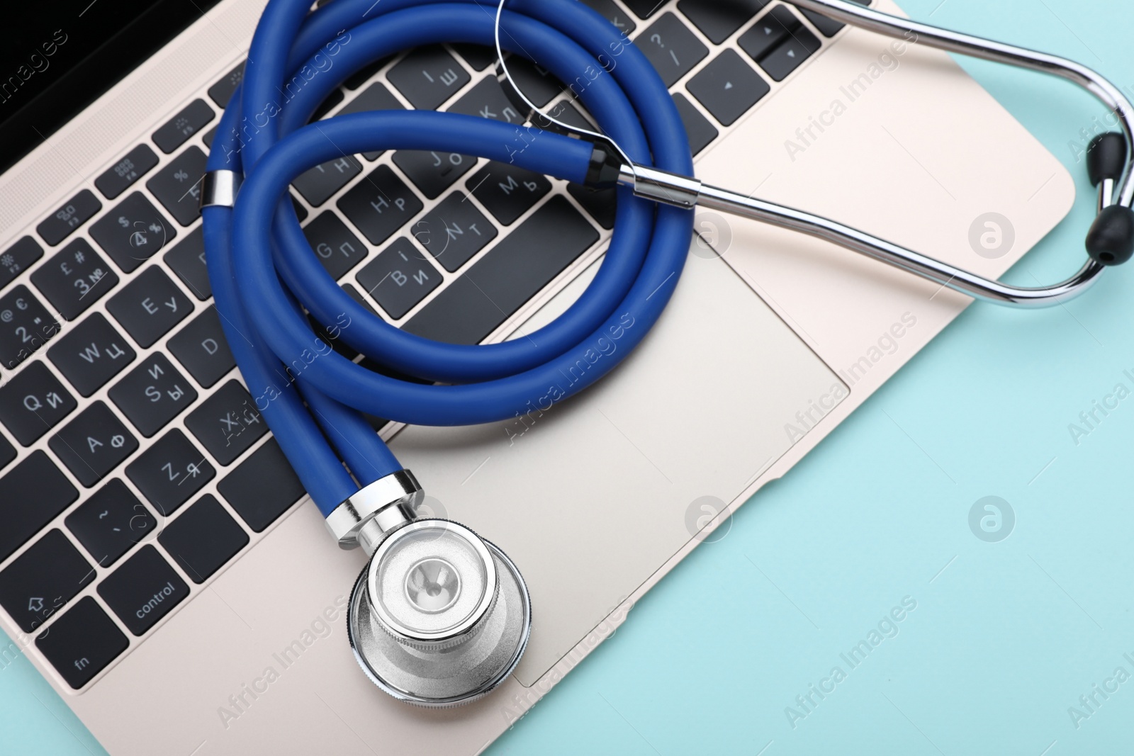 Photo of Laptop and stethoscope on turquoise background, closeup