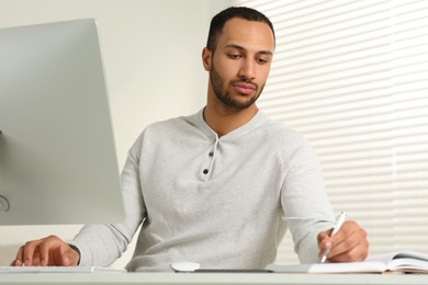 Photo of Young man working on computer at desk in room. Home office