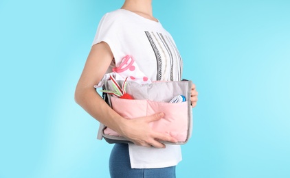 Woman holding maternity bag with baby accessories on color background, closeup