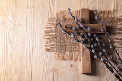 Cross and willow branches on wooden background, flat lay. Space for text
