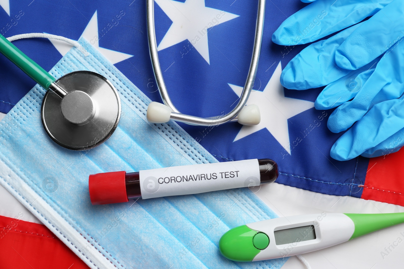 Photo of Test tube with blood, protective mask, gloves, stethoscope and thermometer on American flag, flat lay. Coronavirus pandemic in USA