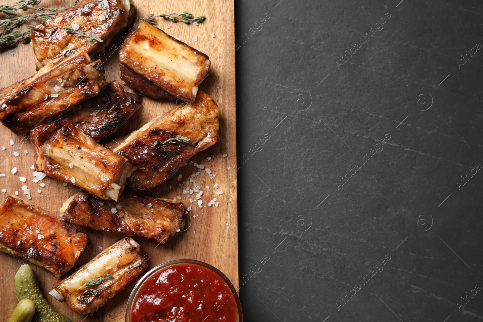 Photo of Delicious grilled ribs served on black table, top view. Space for text