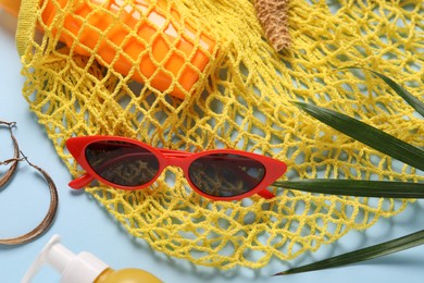 Photo of String bag, different beach accessories and palm leaf on light blue background, flat lay