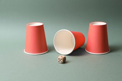 Photo of Three red cups and dice on pale olive background. Thimblerig game