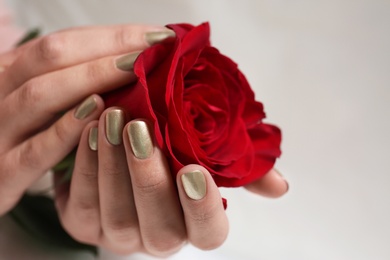 Photo of Woman with gold manicure holding rose on blurred background, closeup. Nail polish trends