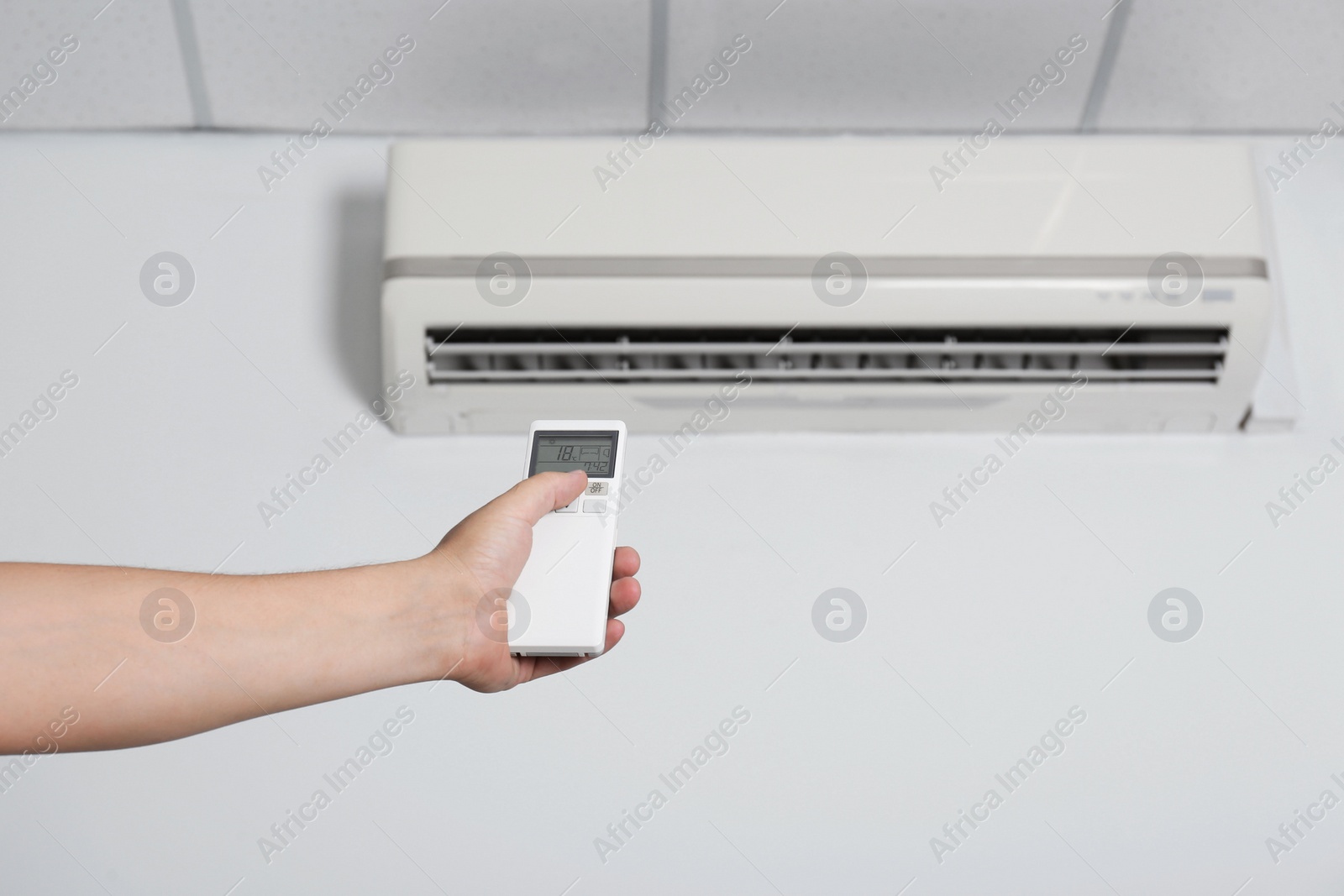 Photo of Man operating air conditioner with remote control indoors, closeup