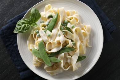 Photo of Delicious pasta with green peas and creamy sauce on black table, top view