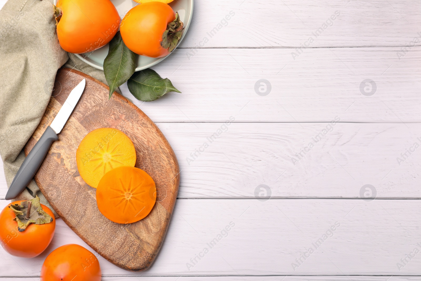 Photo of Delicious ripe juicy persimmons and knife on white wooden table, flat lay. Space for text