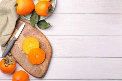 Delicious ripe juicy persimmons and knife on white wooden table, flat lay. Space for text