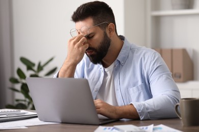 Photo of Man with glasses suffering from headache at workplace in office