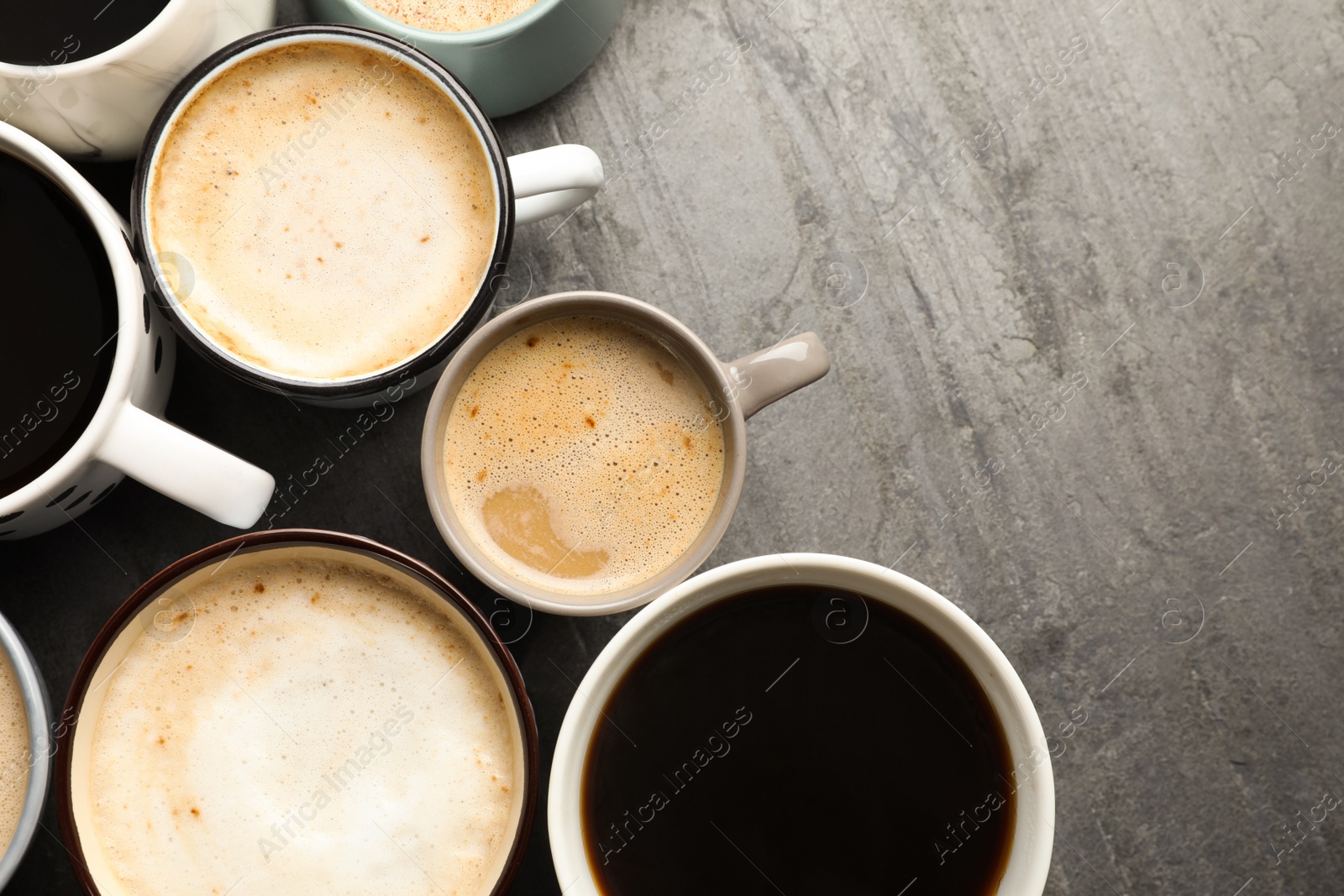 Photo of Many cups of different coffees on slate table, flat lay. Space for text