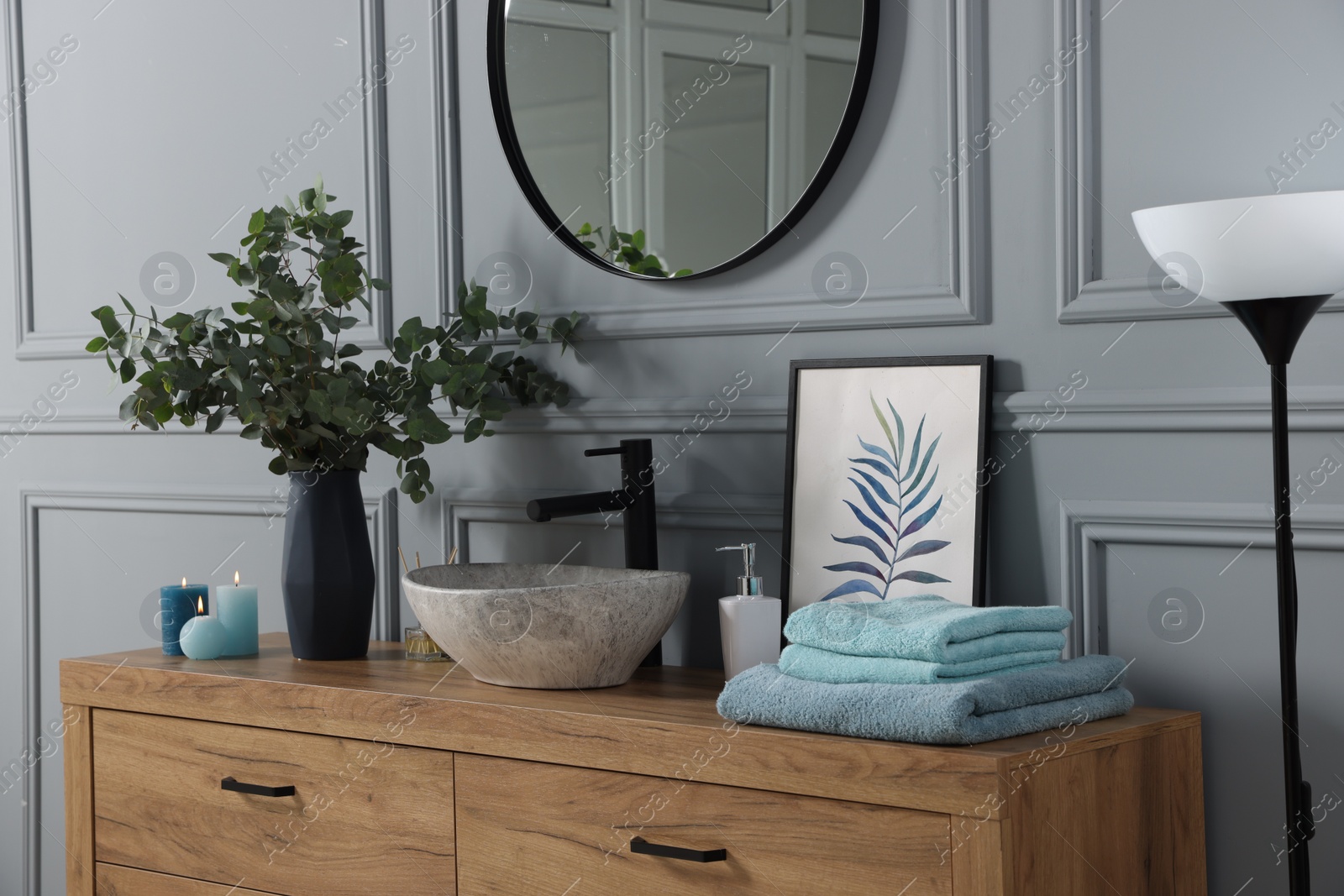 Photo of Folded towels, burning candles and eucalyptus branches near vessel sink on bathroom vanity. Interior design