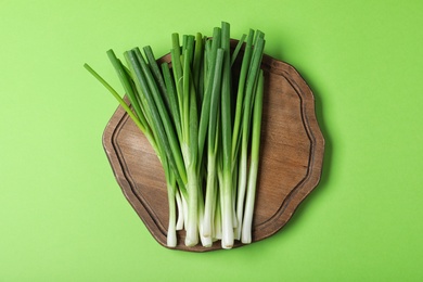 Photo of Wooden board with fresh spring onion on green background