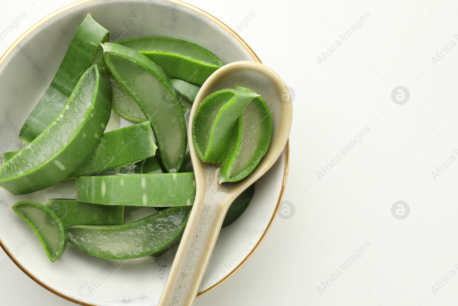 Photo of Bowl with fresh aloe vera pieces and spoon on white table, top view. Space for text