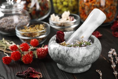 Photo of Mortar with pestle and many different herbs on wooden table, closeup