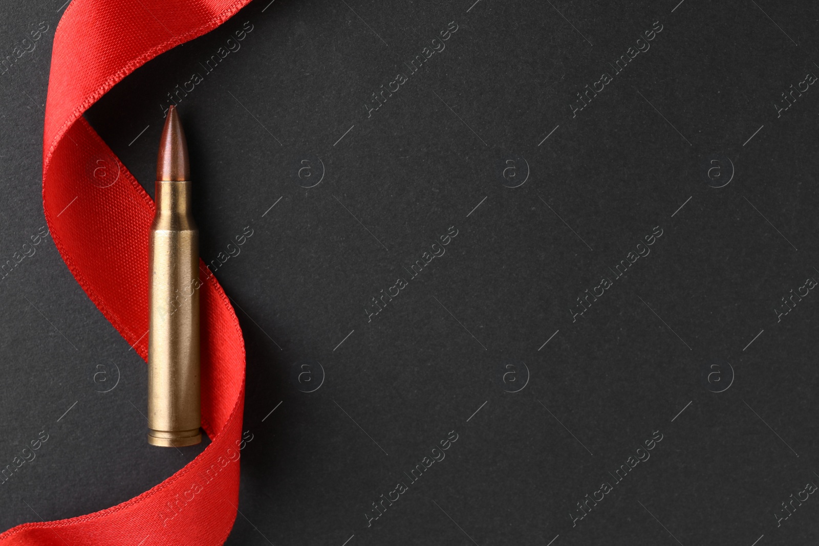 Photo of Bullet and red ribbon on black background, top view. Space for text