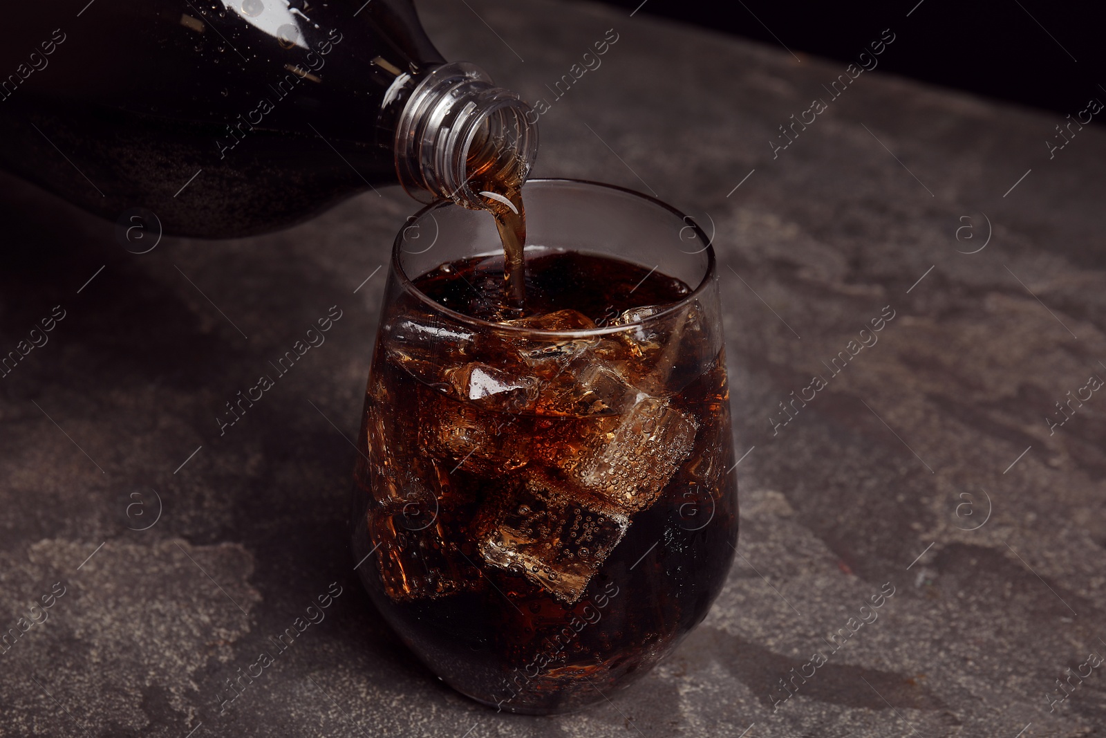 Photo of Pouring refreshing soda drink into glass on grey table