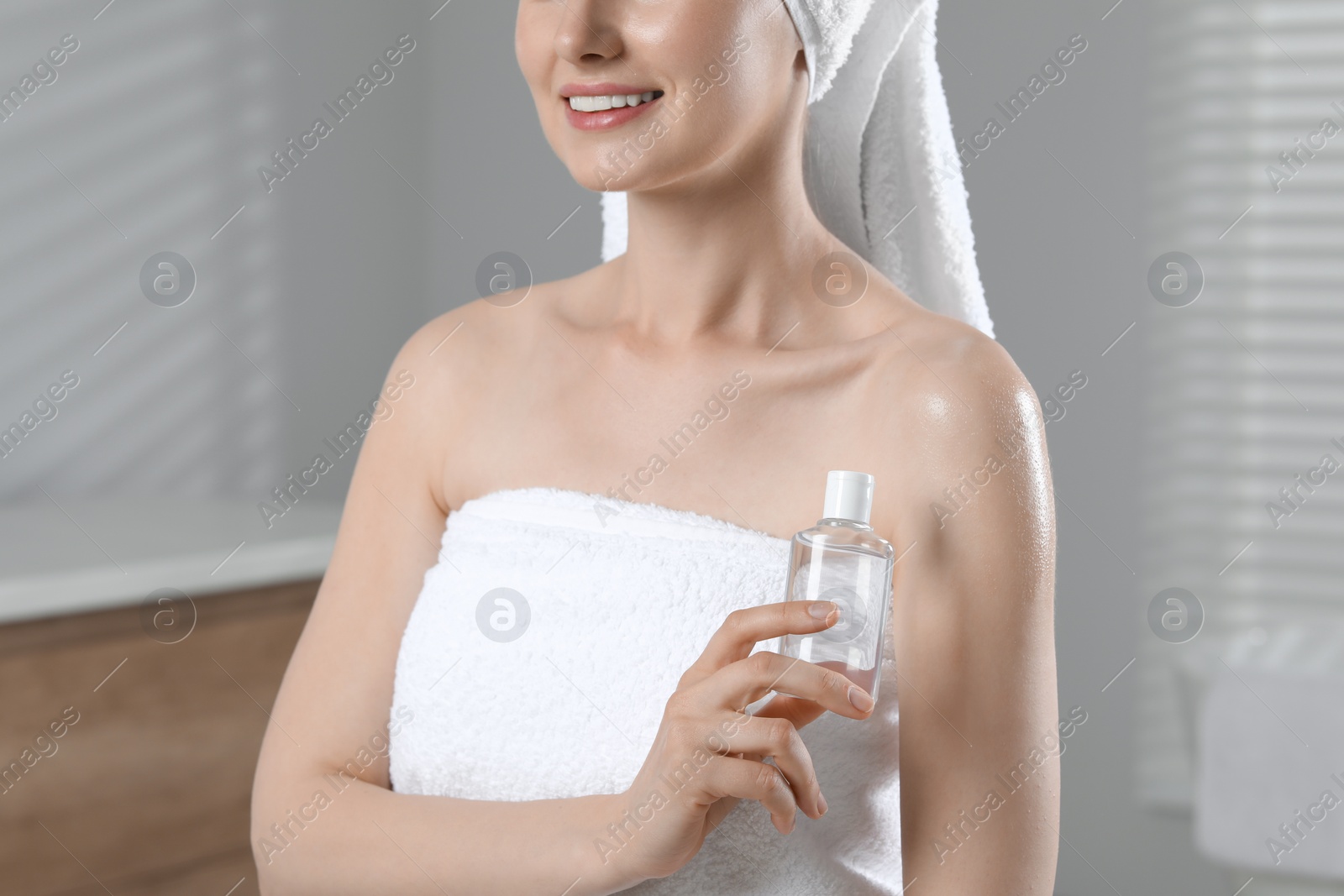Photo of Woman with bottle of body oil in bathroom, closeup