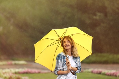 Photo of Happy young woman with umbrella under rain in park