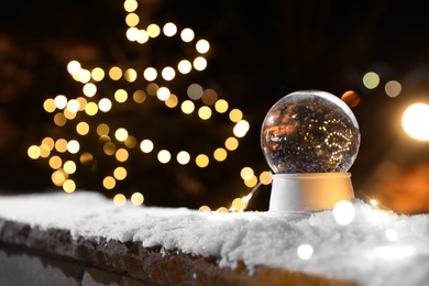 Photo of Snow globe and blurred Christmas lights on background. Space for text