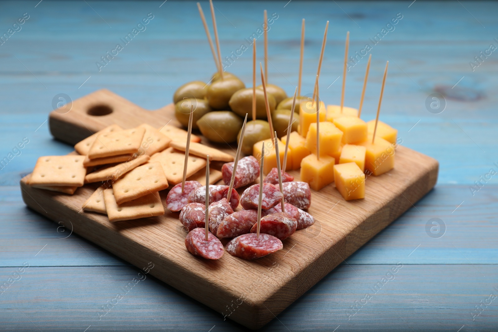 Photo of Toothpick appetizers. Pieces of cheese, sausage, olives and crackers on light blue wooden table, closeup