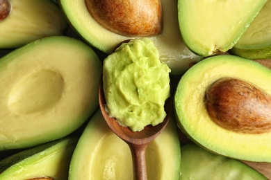 Photo of Spoon with guacamole on ripe avocados, top view