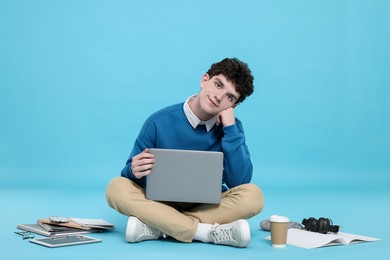Portrait of student with laptop and stationery on light blue background