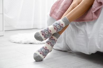 Woman wearing knitted socks on bed indoors, closeup. Warm clothes