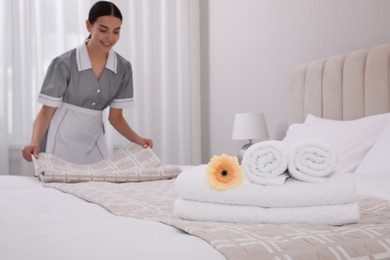 Photo of Chambermaid making bed in hotel room, focus on fresh towels. Space for text