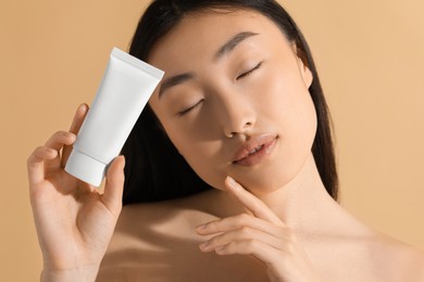 Photo of Beautiful young woman holding sun protection cream on beige background, closeup