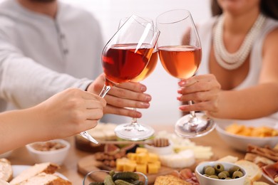 Photo of People clinking glasses with rose wine above wooden table indoors, closeup