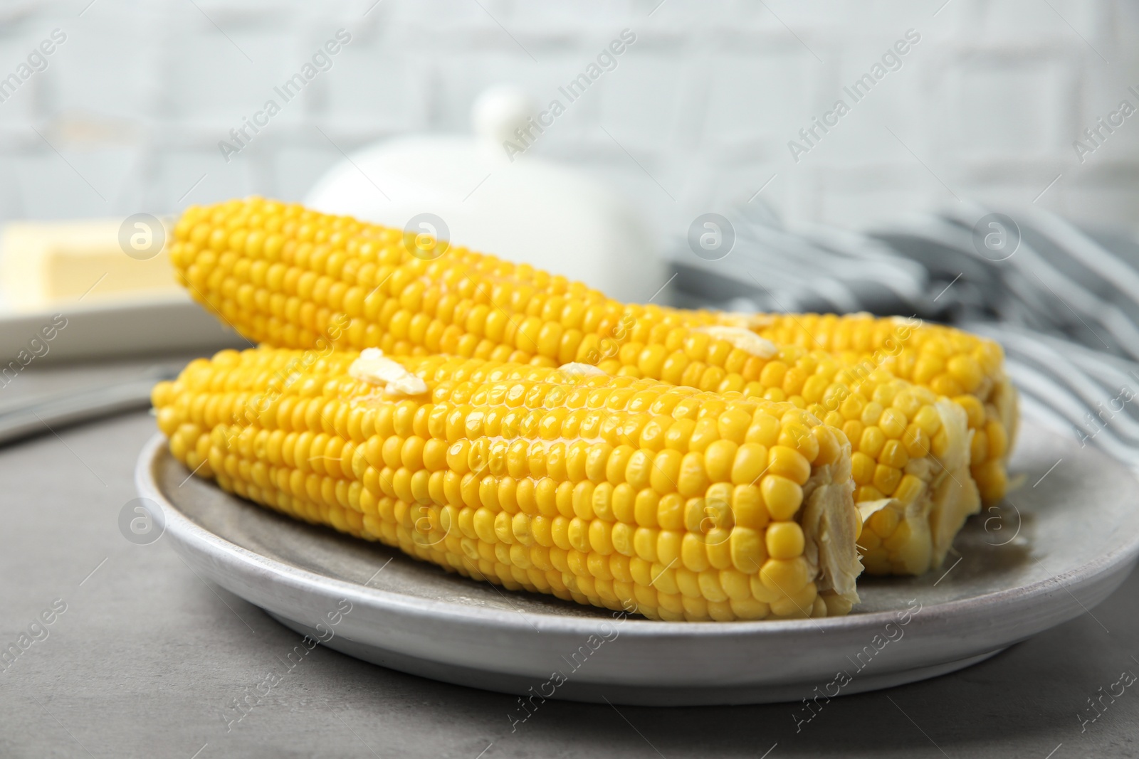 Photo of Plate of tasty boiled corn cobs with butter on light grey table