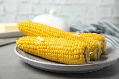 Photo of Plate of tasty boiled corn cobs with butter on light grey table