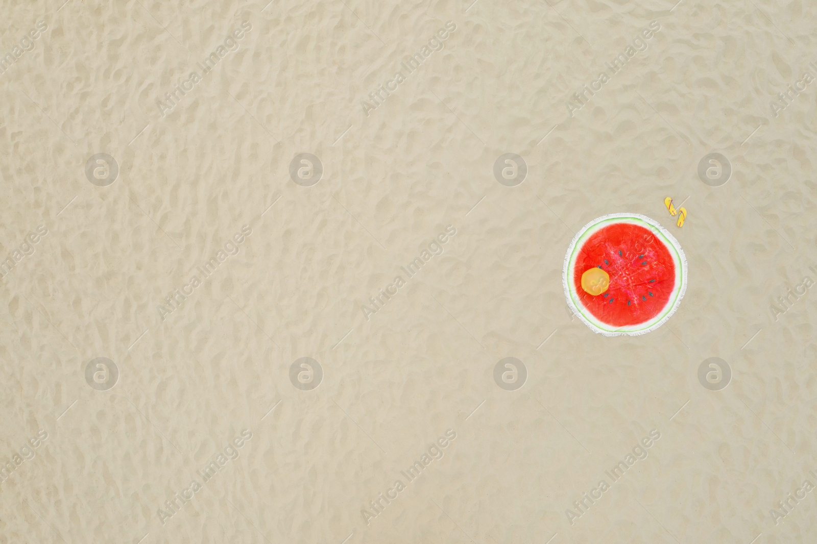 Image of Round watermelon beach towel, ball and flip flops on sand, aerial view. Space for text