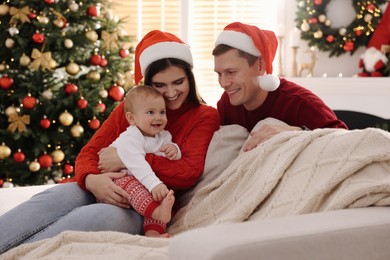 Photo of Happy couple with cute baby on sofa in room decorated for Christmas