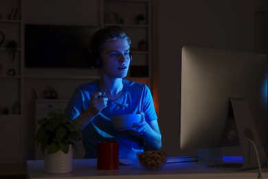 Photo of Teenage boy eating porridge while using computer in room at night. Internet addiction