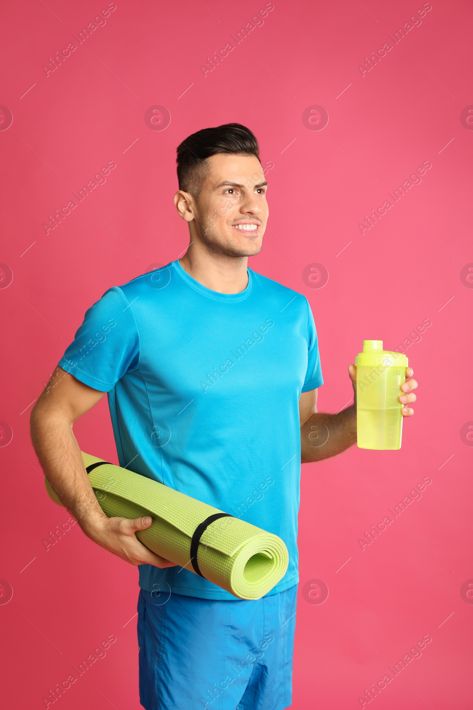 Photo of Handsome man with yoga mat and shaker on pink background