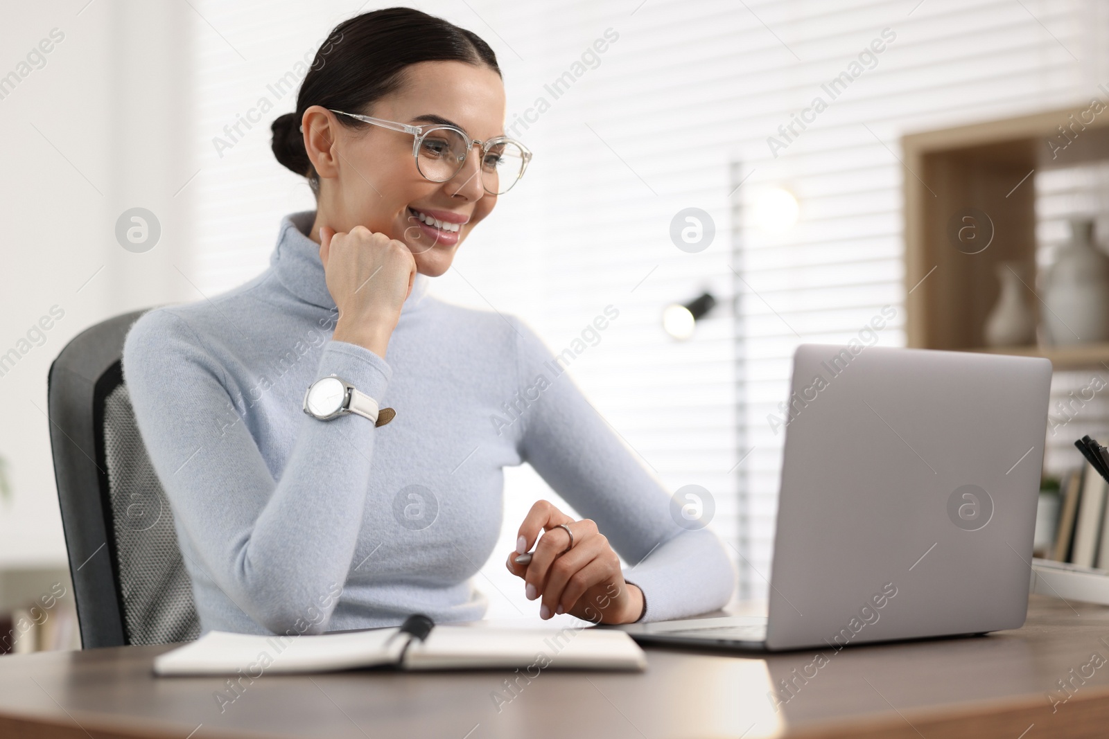 Photo of Young woman in glasses watching webinar at table in office