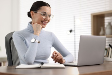 Photo of Young woman in glasses watching webinar at table in office