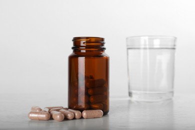Photo of Gelatin capsules, bottle and glass of water on white wooden table